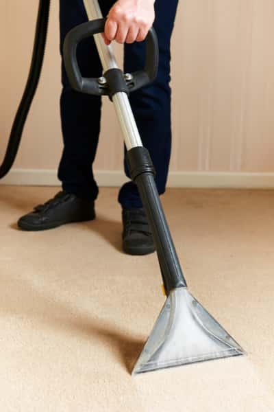 This is a photo of a man steam cleaning a cream carpet, using a professional steam cleaning machine.