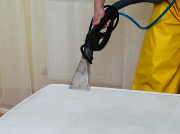 This is a photo of a man steam cleaning a dirty mattress.