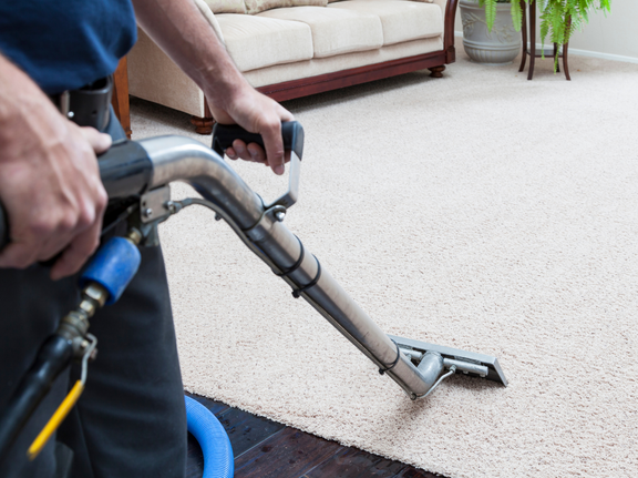 This is a photo of a man with a steam cleaner cleaning a cream carpet.
